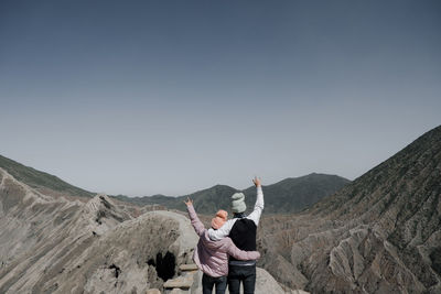 Rear view of couple gesturing while standing on cliff at rocky mountain