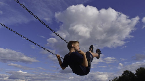 Low angle view of boy swinging against sky