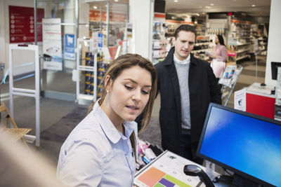 Saleswoman discussing with male customer at cash counter in electronics store