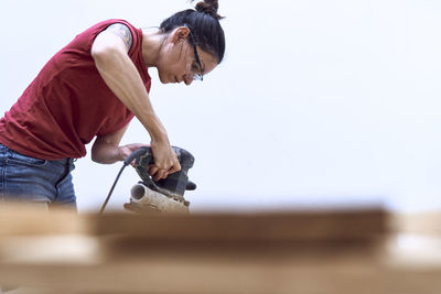 Young woman polishing a wooden plank with a power sander