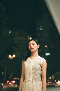 Young woman standing against illuminated tree at night