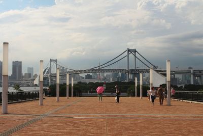 People walking in city against cloudy sky