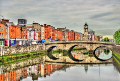 Bridge over river by buildings against sky in city