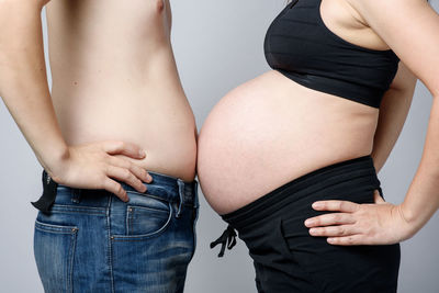 Midsection of husband and pregnant wife standing over gray background