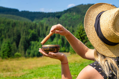 Rear view of woman holding hat standing on field