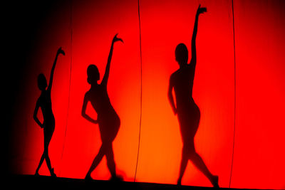 Silhouette people dancing against orange sky