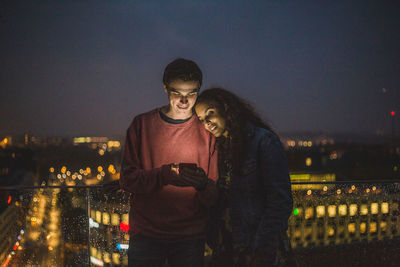 Young man and woman standing in city against sky at night