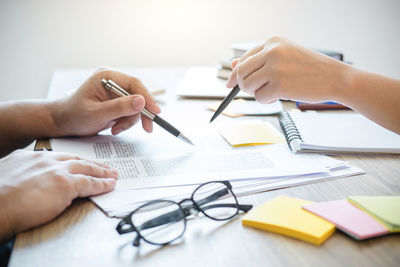 Cropped hands of friends with pens studying on desk at home