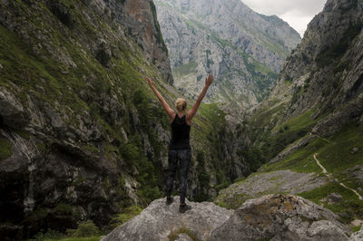 Rear view of woman with arms raised standing on rock amidst mountains