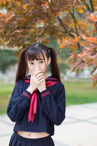 Portrait of young woman standing by tree during autumn