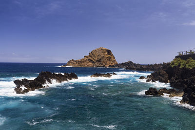 Rock formation in sea against clear blue sky