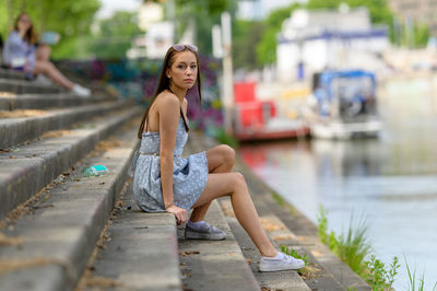 A portrait of a pretty young woman taken in the summertime in a city sitting on a staircase.