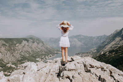 Woman standing on rock by mountains against sky