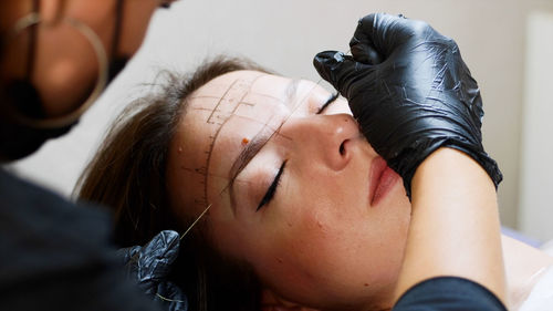 Cropped hands of beautician threading woman eyebrow