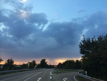 Road by trees against sky during sunset