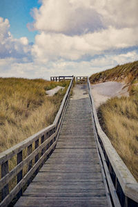 Boardwalk amidst grass against sky