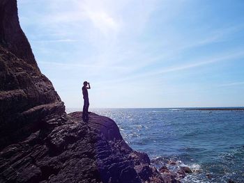 Man standing on rock by sea against sky