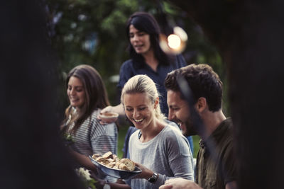 Happy woman holding bread bowl while enjoying dinner party with friends at yard