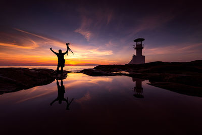 Silhouette man standing on rock against sky during sunset