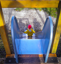 Rear view of boy sitting on yellow slide at playground