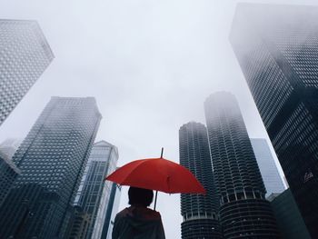 Woman with red umbrella standing in front of modern office blocks
