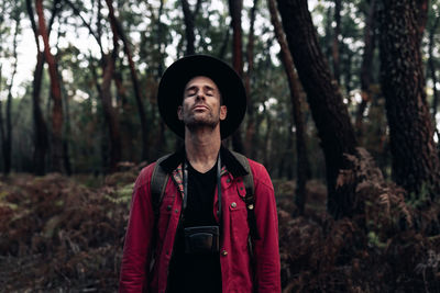 Adult traveler in hat closing eyes and breathing peacefully in harmony with nature of forest