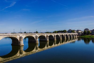 Arch bridge over river against blue sky