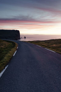 Road by sea against sky during sunset