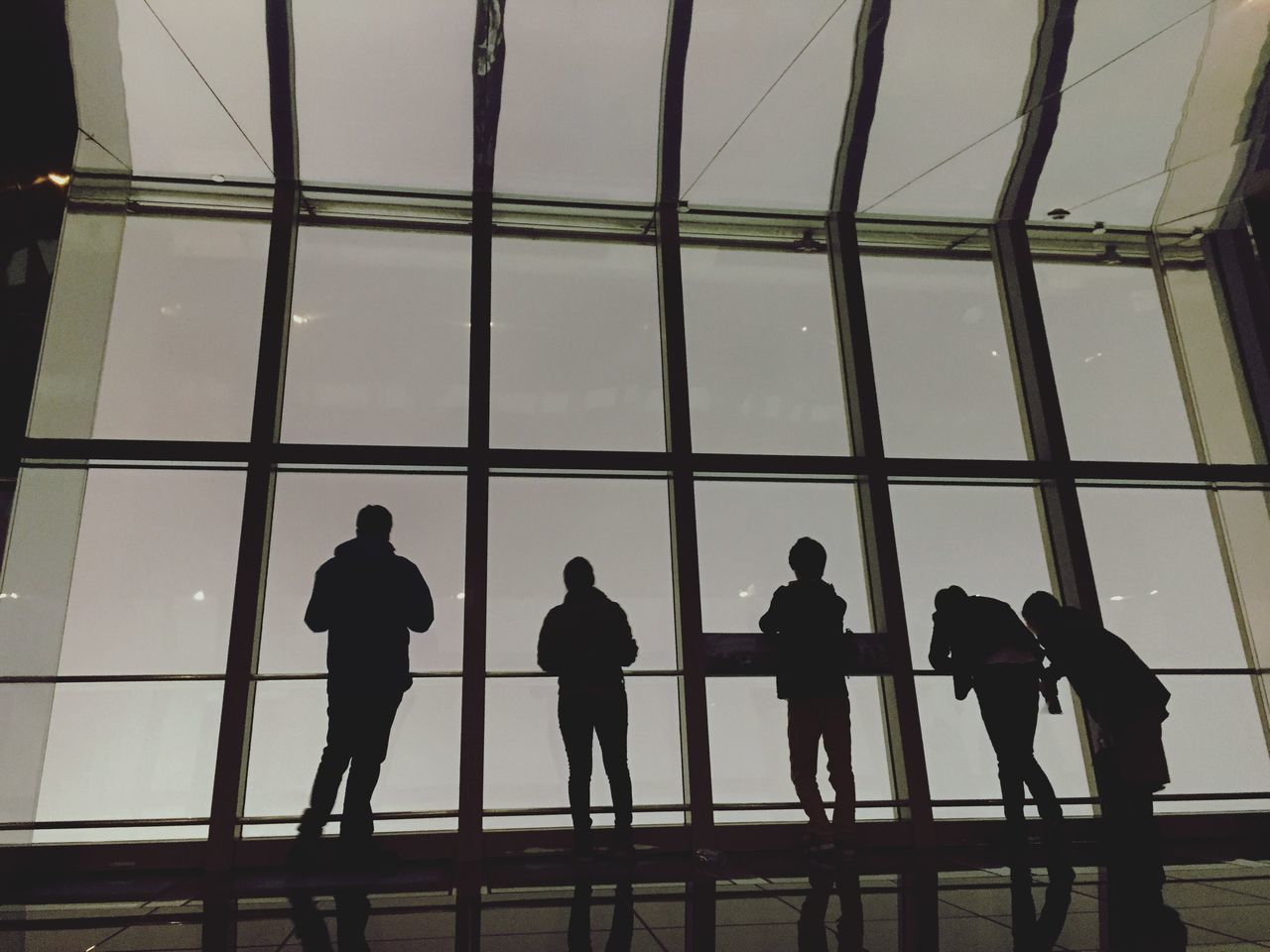 men, silhouette, indoors, lifestyles, person, togetherness, standing, walking, architecture, built structure, glass - material, leisure activity, full length, railing, window, medium group of people, side by side