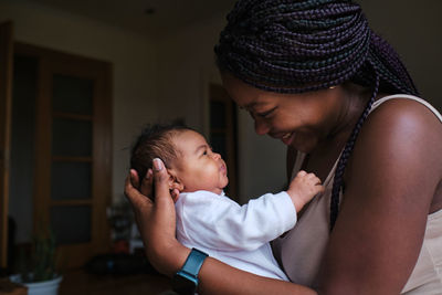 Side view of loving african american mom cuddling and holding newborn baby while enjoying pleasant motherhood moments