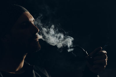 Portrait of young man smoking cigarette against black background