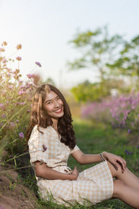 Young woman smiling while sitting by tree against plants