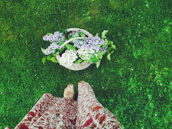 Low section of woman standing by flower basket on grassy field