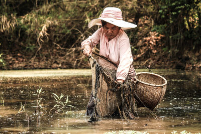 Mature woman with fishing net and basket standing in lake