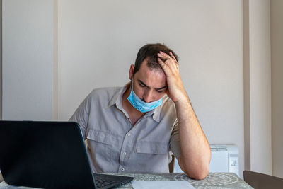 Frustrated man wearing flu mask sitting at office