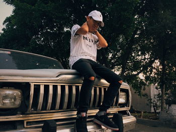 Full length of young woman sitting on car