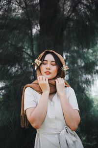 Beautiful young woman with eyes closed against trees in forest