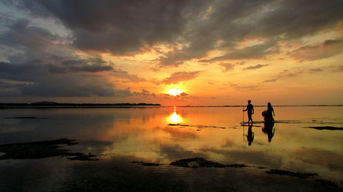 Silhouette people on beach against sky during sunset