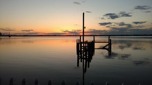 Silhouette wooden posts in lake against sky at sunset