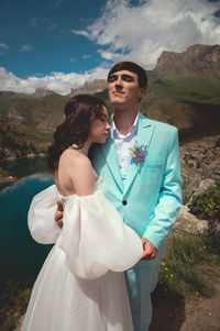 Beautiful wedding couple hugs tenderly against the backdrop of a mountain river and lake, the bride