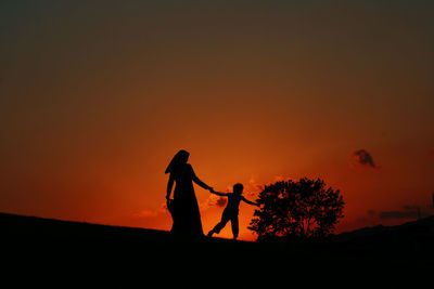 Silhouette girls standing on land against orange sky