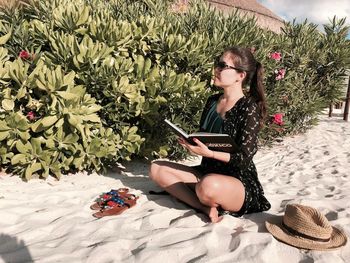 Woman reading book while sitting on sand at beach