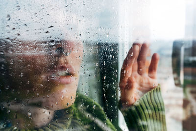 Close-up portrait of woman seen through wet window in rainy season