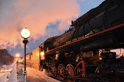 Train on illuminated railroad tracks against sky during sunset