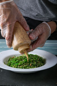 Close-up of person pouring green salad in plate on table