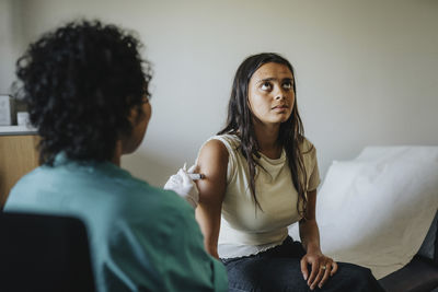 Female doctor giving vaccine to young woman sitting in clinic