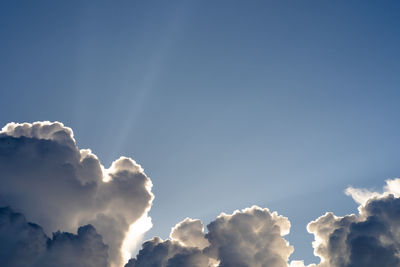 Low angle view of sunlight streaming through clouds