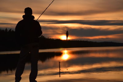 Silhouette man fishing on lake against sky during sunset