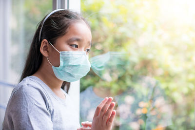 Girl wearing mask looking through window at home