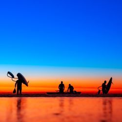 Silhouette people on beach against clear sky during sunset